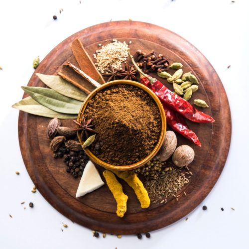 Indian Garam masala powder in bowl and it's ingredients colourful spices. Served over moody background. selective focus