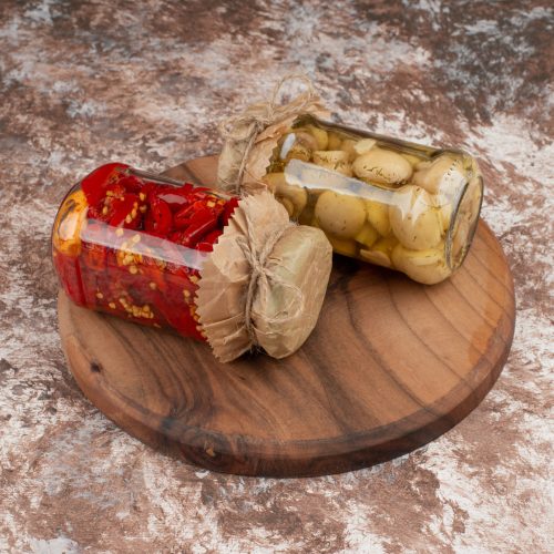 Pickled red peppers and mushrooms in a glass jar on wooden plate. High quality photo