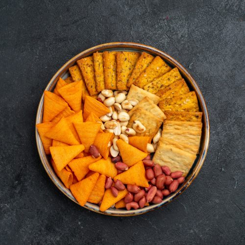 top-view-different-snacks-crackers-nuts-crisps-dark-grey-surface